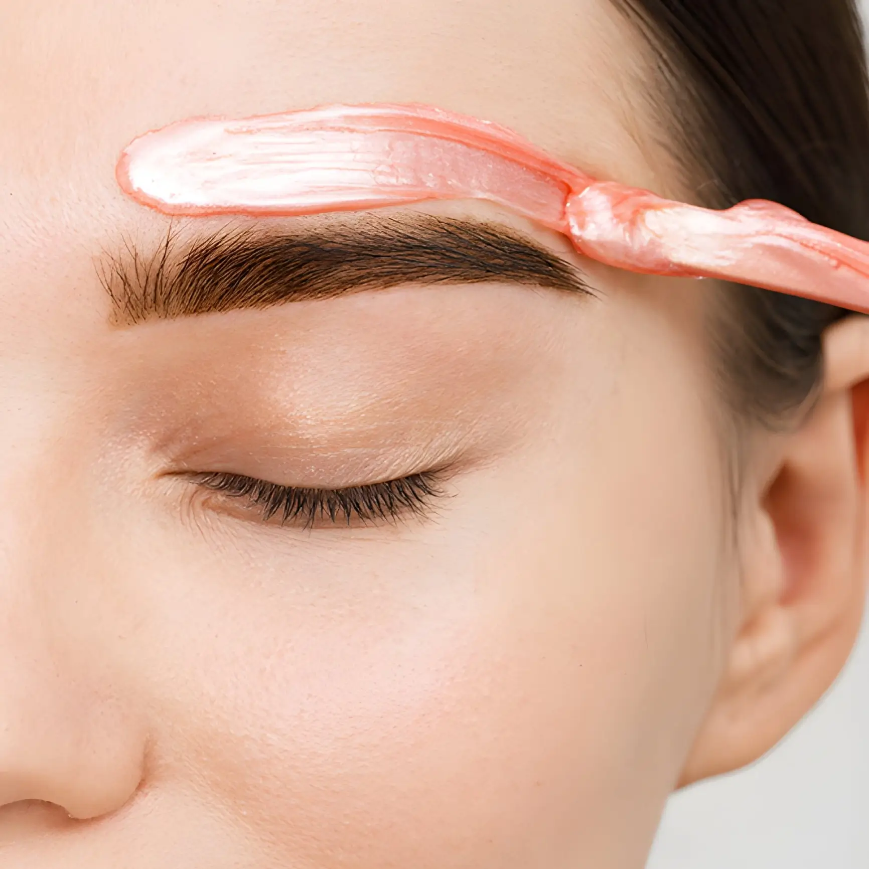 Eyebrow with pink cream being applied.